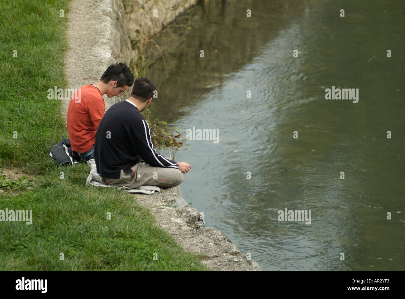 Two Youths Sitting on a River Embankment Stock Photo