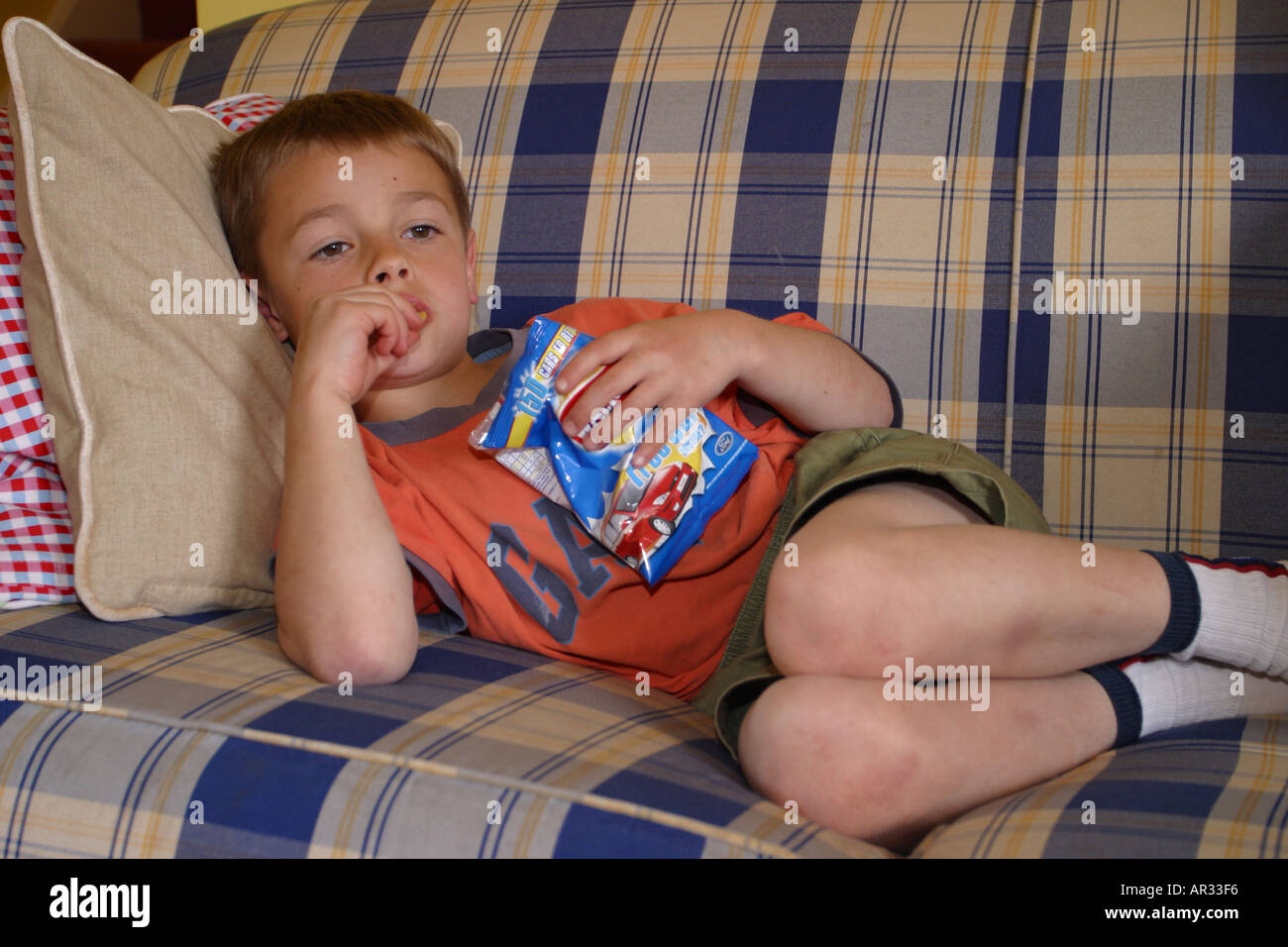 Young Boy under 10 lying on a sofa watching television TV and eating potato crisps Stock Photo
