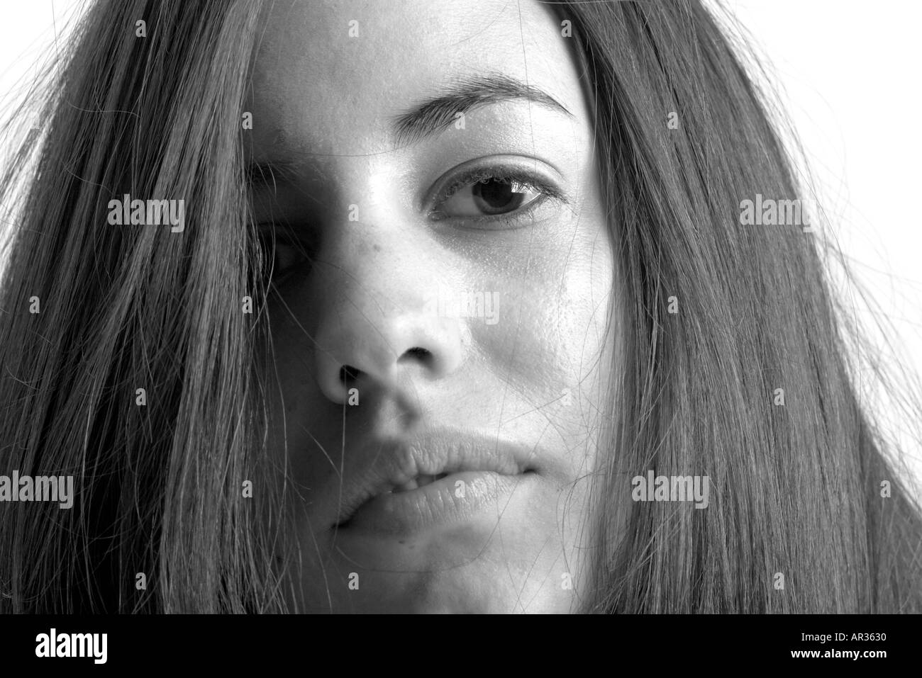 Black and white headshot of young black haired woman looking down at the camera with her hair covering one eye Stock Photo