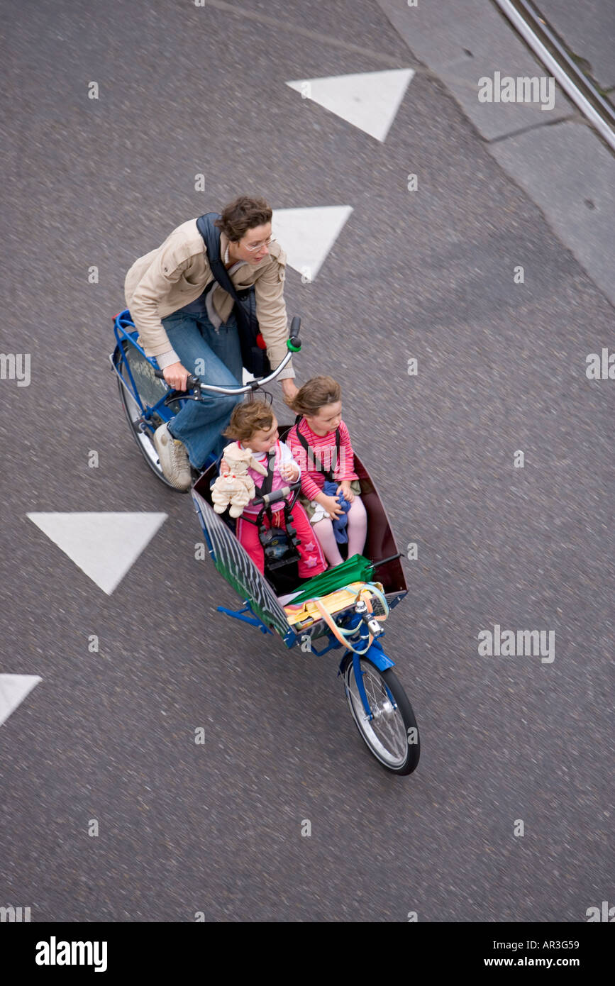 HOLLAND AMSTERDAM MOTHER WITH TWO CHILDREN ON A CARGO BIKE CYCLING OVER WHITE TRIANGLES SIGN PAINTED ON THE ROAD Stock Photo