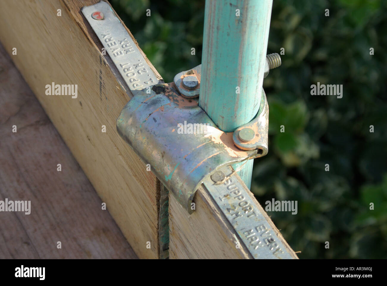 Close up of scaffold connection clip holding vertical timber toe board