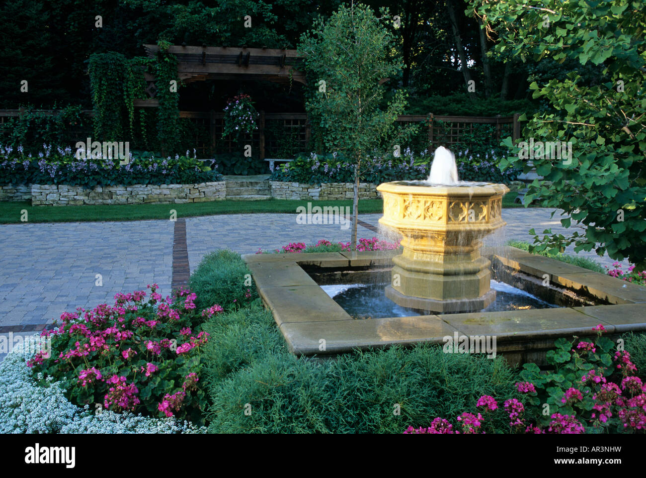 GARDEN FOUNTAIN AT LUXURY MINNESOTA HOME SURROUNDED BY PERENNIALS.  GINGKO TREE AT RIGHT; ARBOR IN BACKGROUND.  SUMMER. Stock Photo