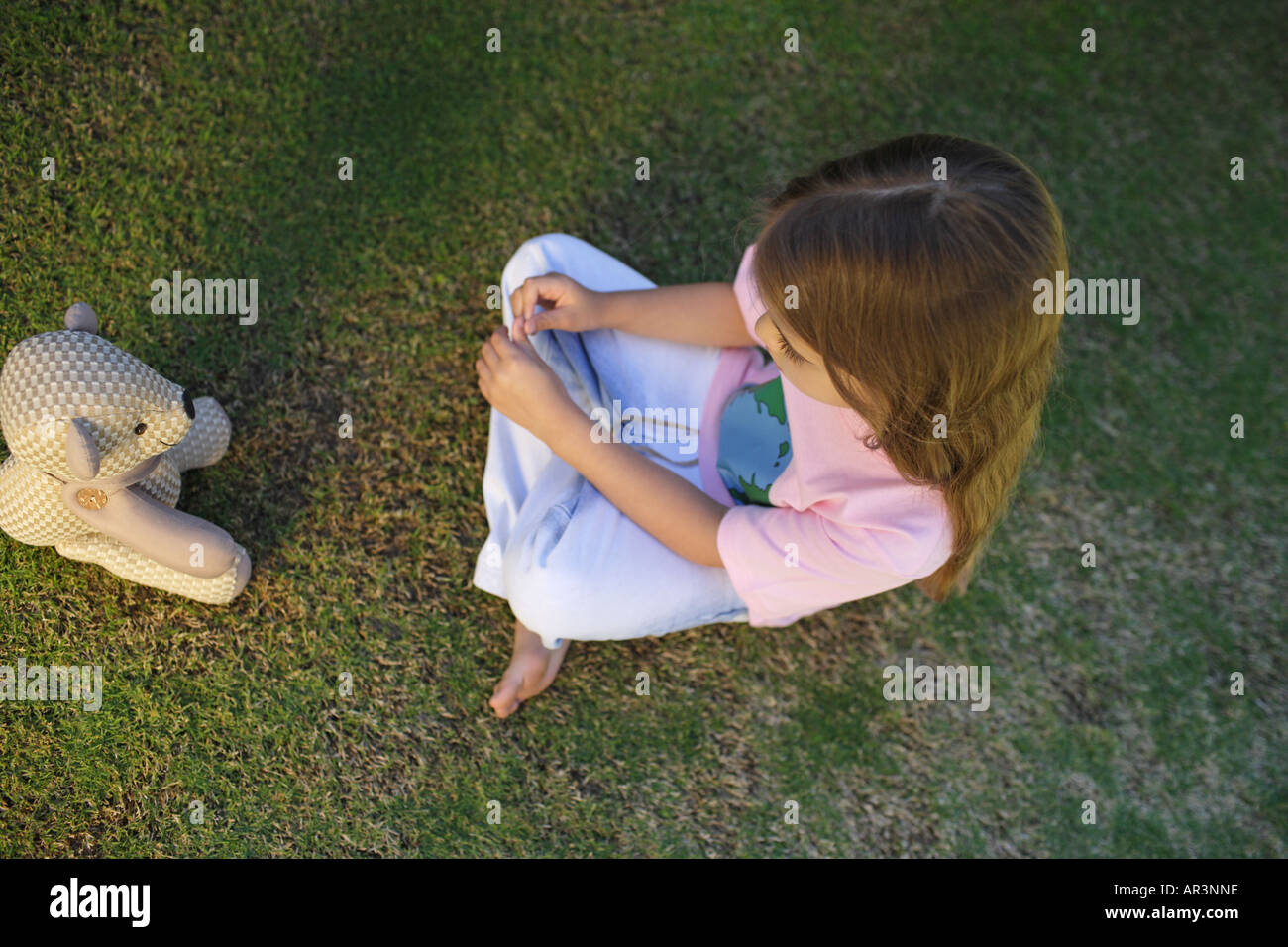 Young girl sitting on grass opposite toy bear Stock Photo - Alamy