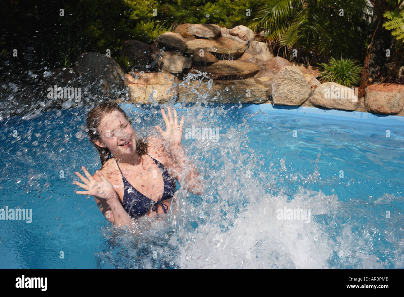 Young woman being splashed in outdoor swimming pool Stock Photo