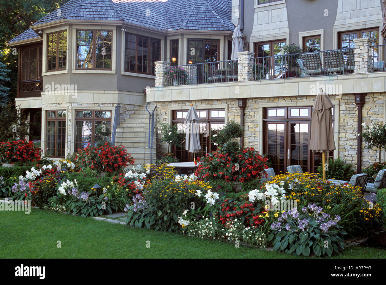 BACK VIEW OF TWO-LEVEL LAKE HOME IN MINNESOTA, INCLUDING UPPER DECK AND LOWER PATIO WITH BORDER GARDEN OF PERENNIALS. SUMMER. Stock Photo