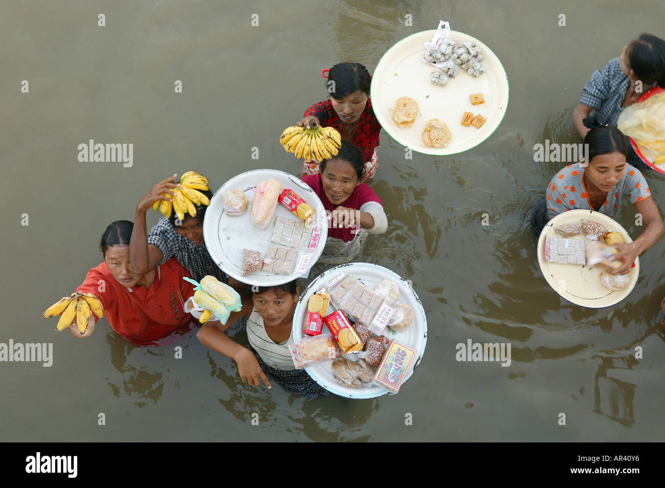 Women vendors standing waist-high in river, carrying fruit, Myanmar Stock Photo