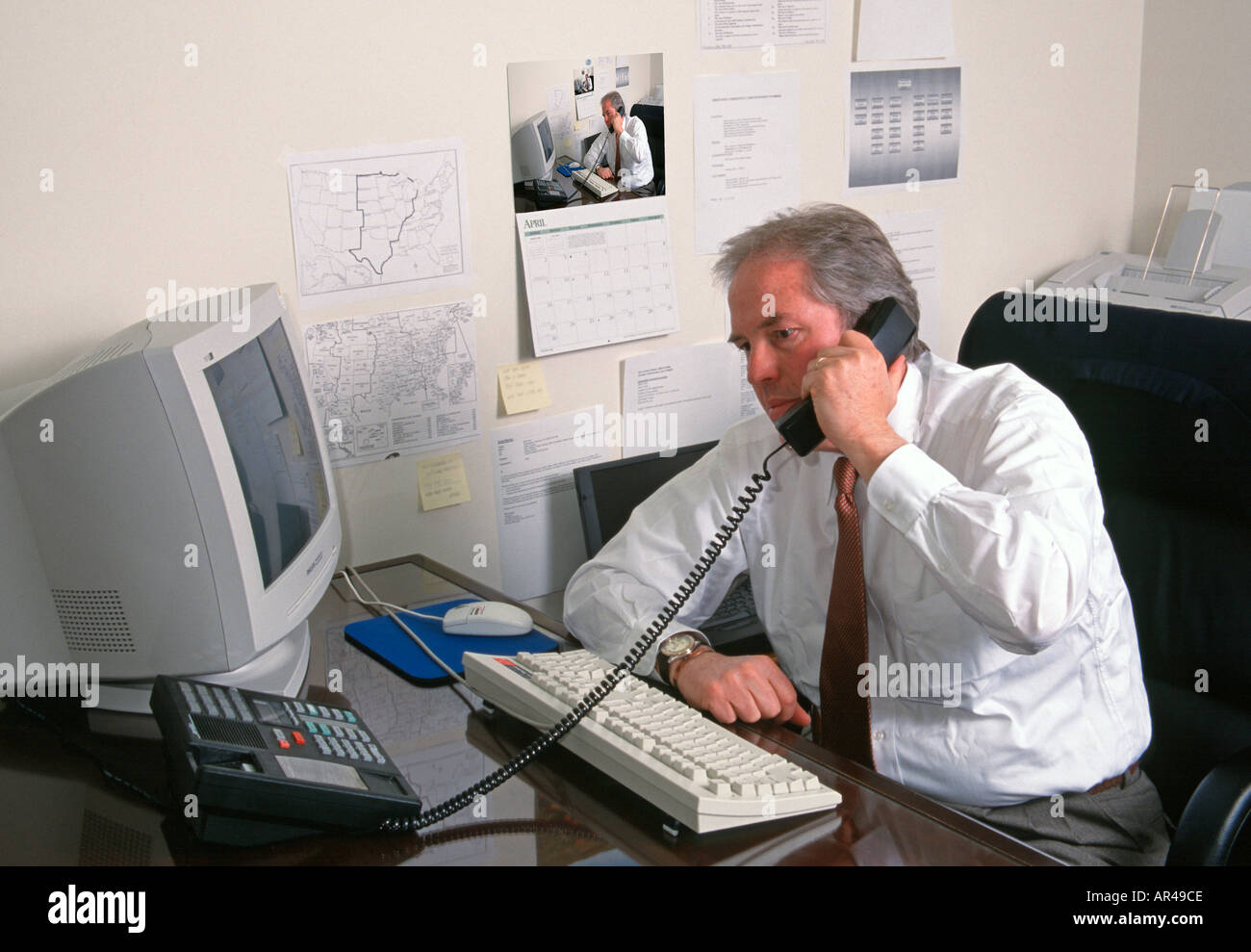 Middle aged white male executive sitting at desk talking on telephone Calendar has same image convergent series Stock Photo