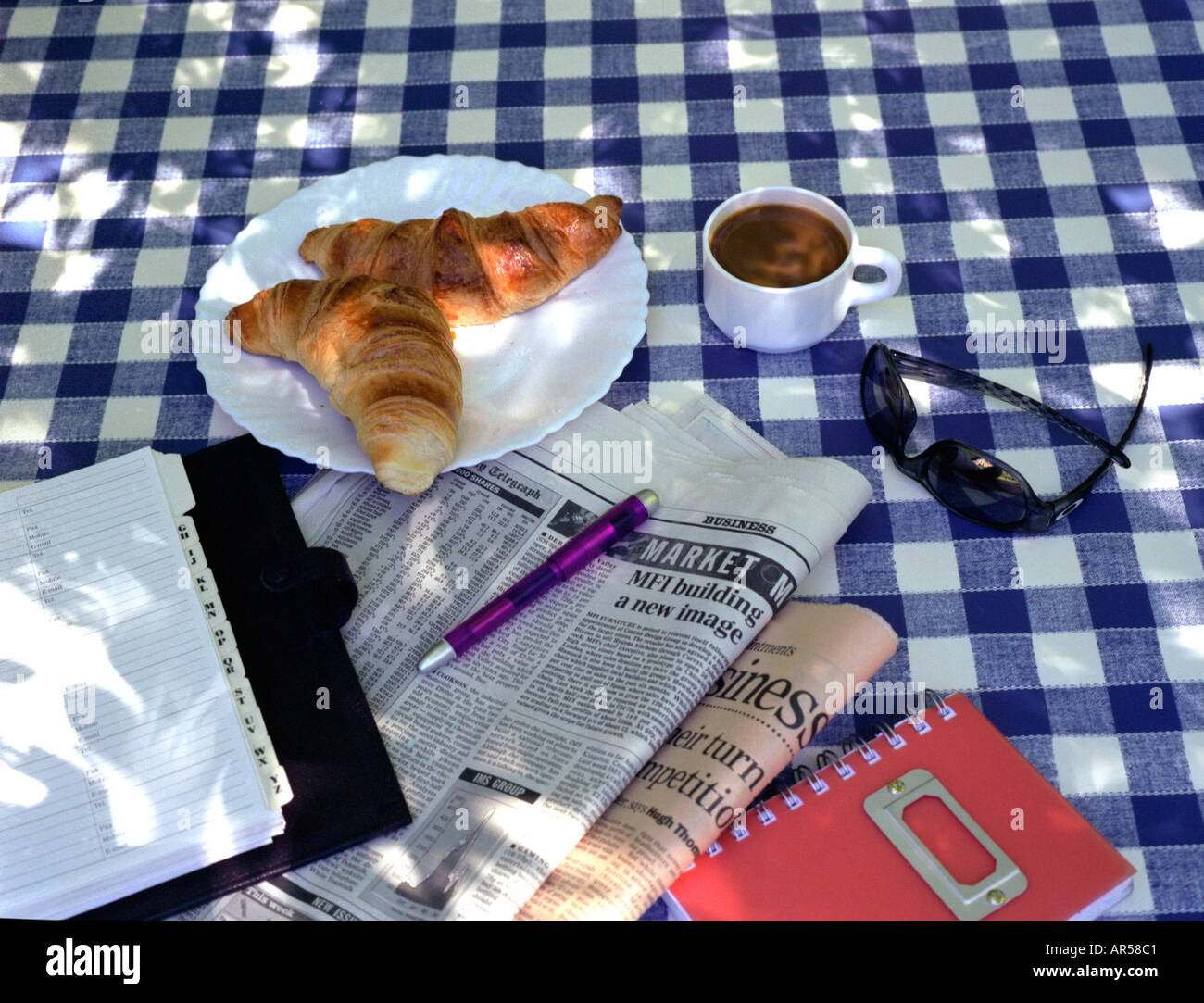 newspaper coffee and croissants under the shade of a tree in summer Stock Photo