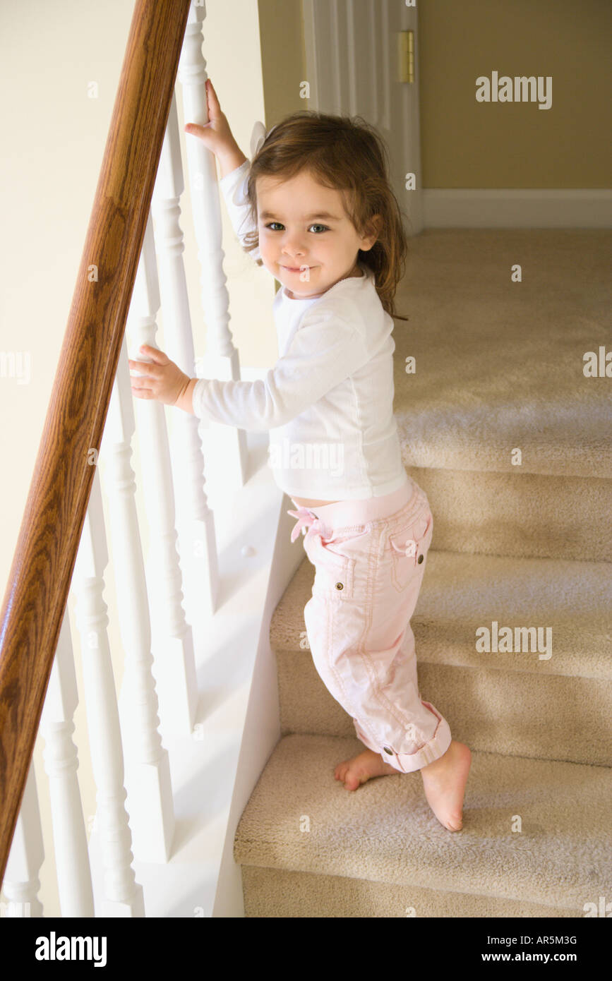 Caucasian girl toddler standing on carpeted stairs holding onto railing