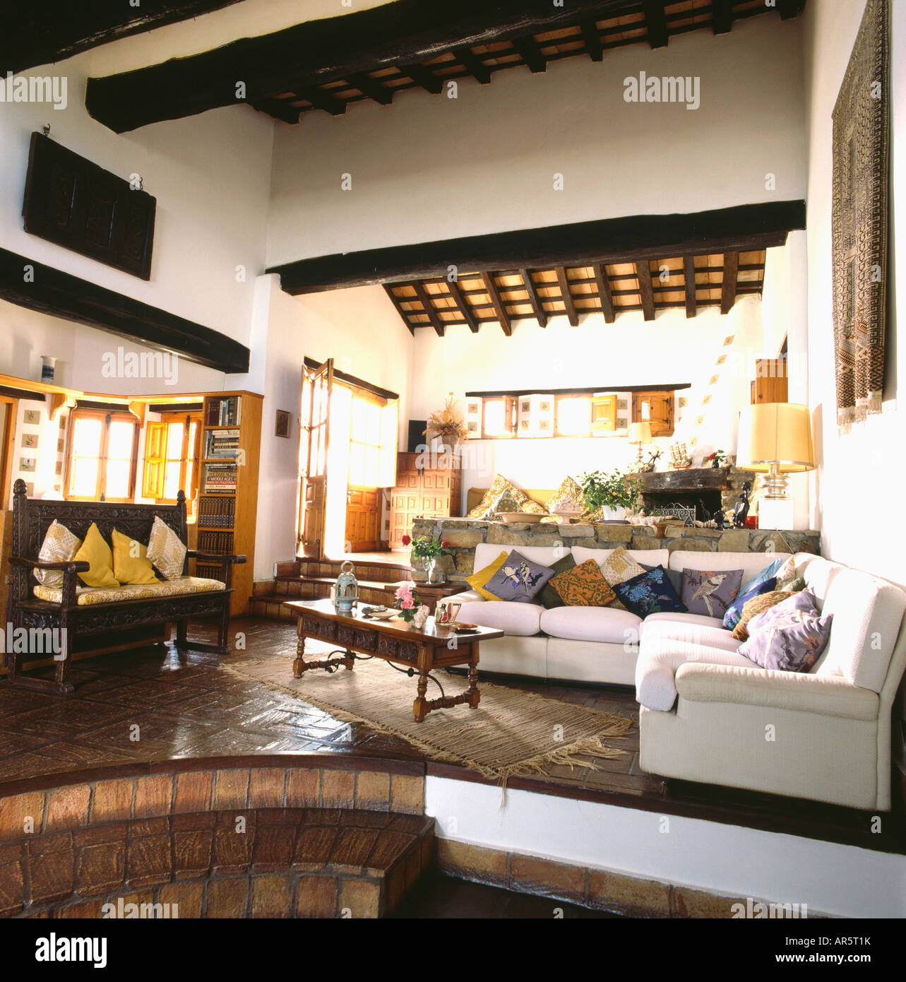 Wooden settle and white L shaped sofa in seventies Spanish living room with  beamed ceiling and tiled floor and steps Stock Photo - Alamy