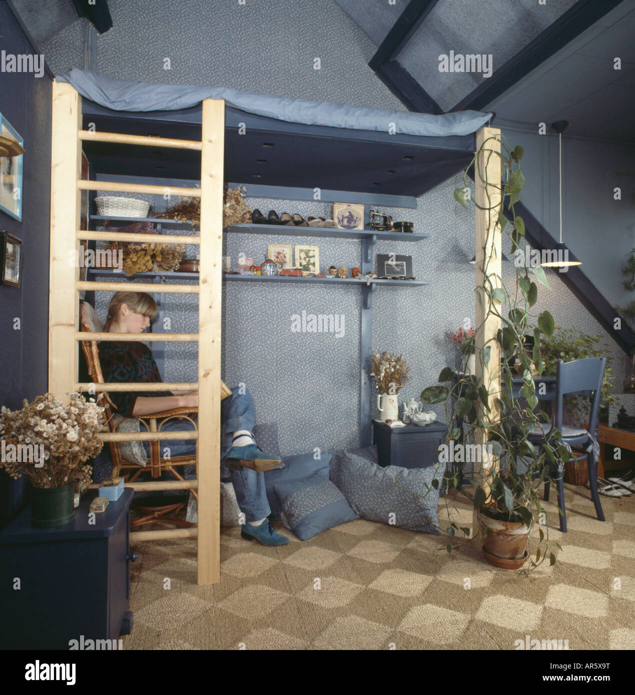 Teenager reading below platform bed in blue sixties bedroom with rush
