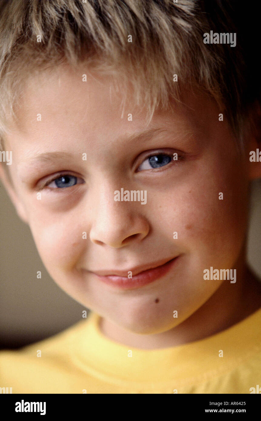 Male child blonde spiky hair wearing yellow t shirt looking to camera smiling Stock Photo