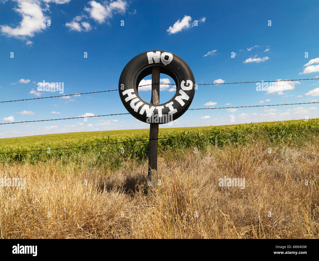 Barbed wire fence with tire reading No Hunting in front of agricultural field Stock Photo