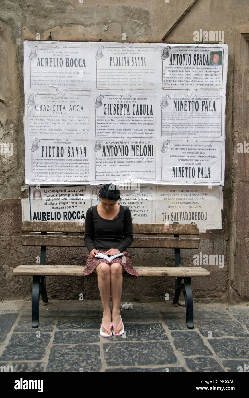 Woman reading book below posters on wall in village of Bosa in Sardinia Italy 2007 Stock Photo