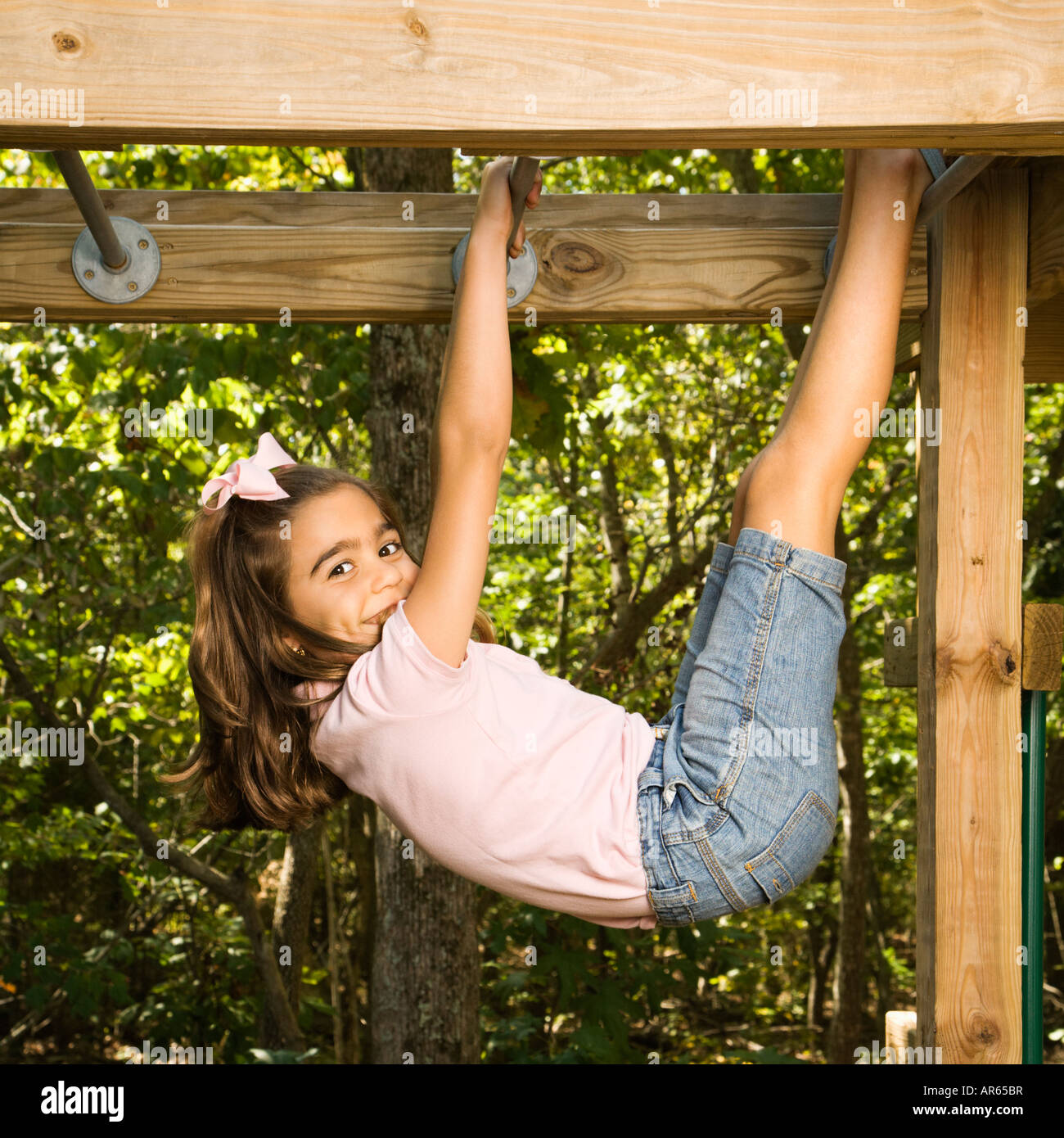 Side view of Hispanic girl hanging by arms and legs from monkey bars
