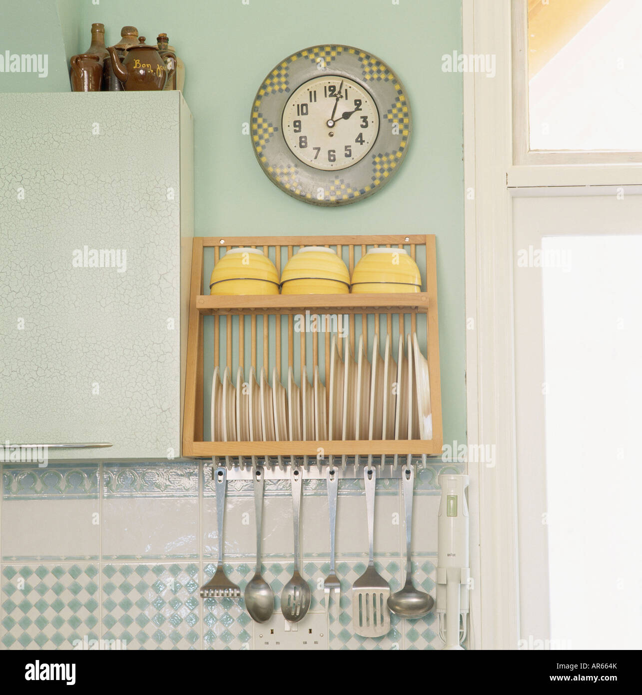 Clock above plate rack with stainless steel utensils stored below Stock Photo