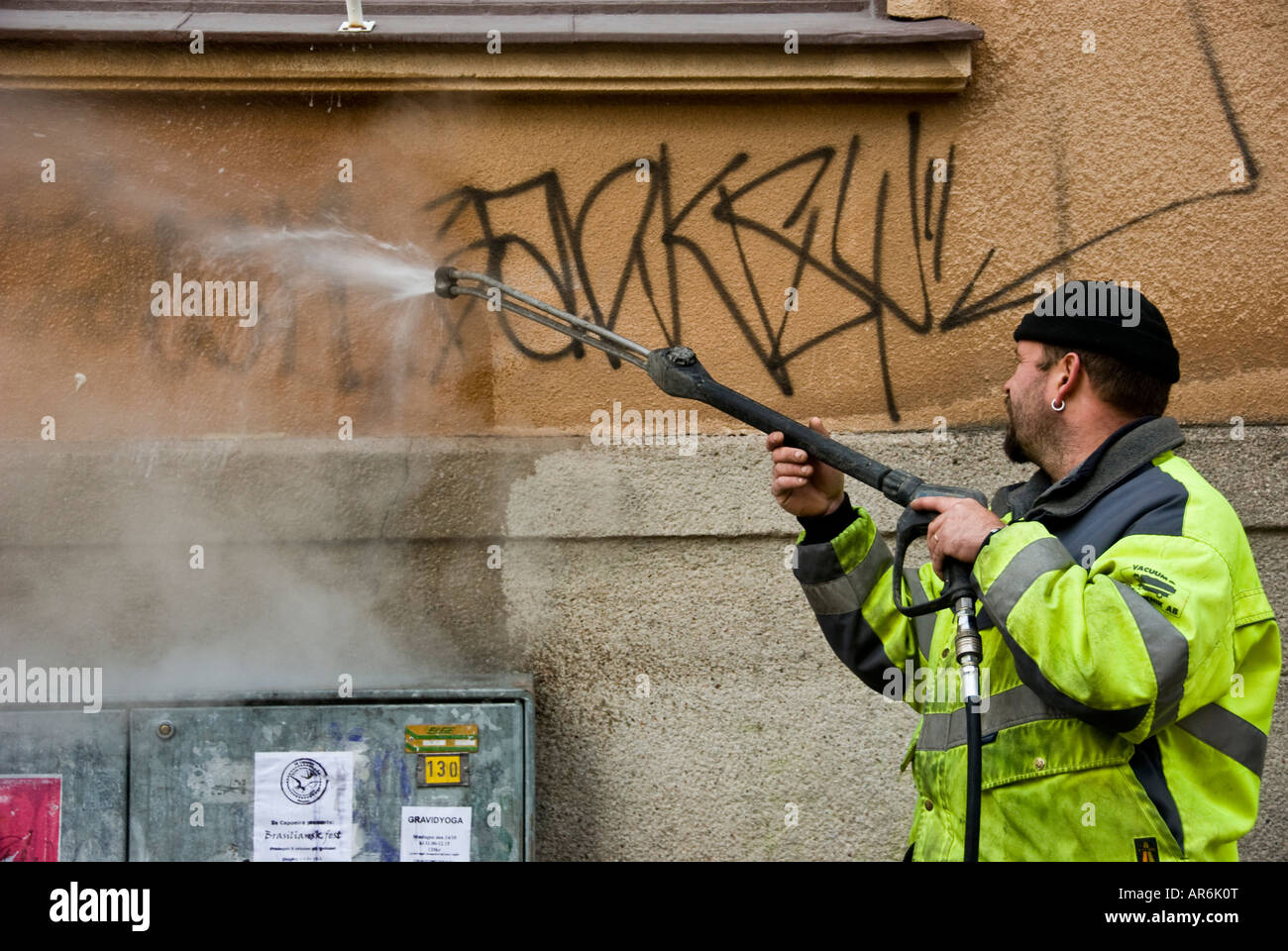 A sanitation worker tries to clean away graffiti from a wall with a high pressure water hose Stock Photo