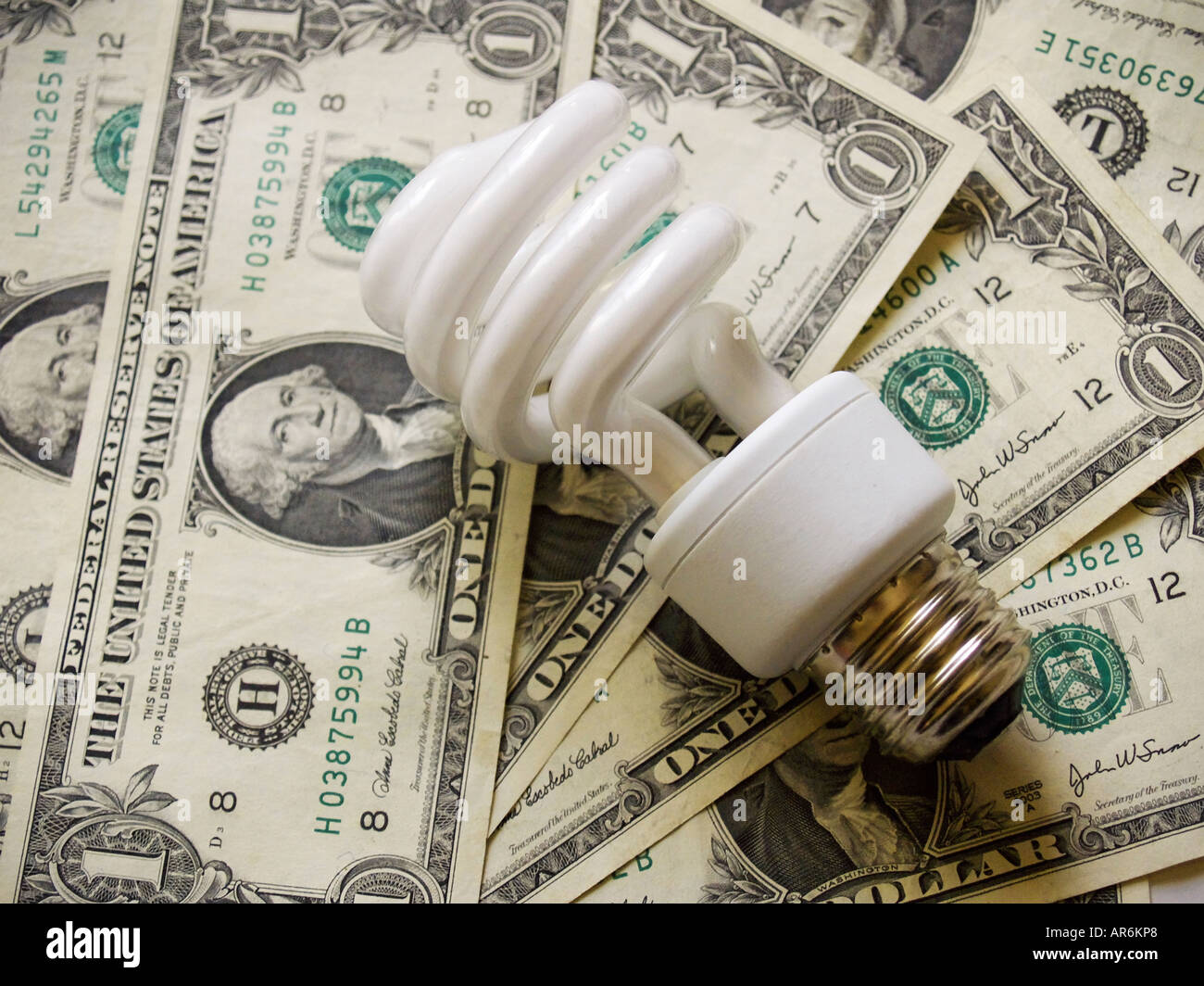 Spiral shaped fluorescent light bulb against a background of dollar bills. Stock Photo