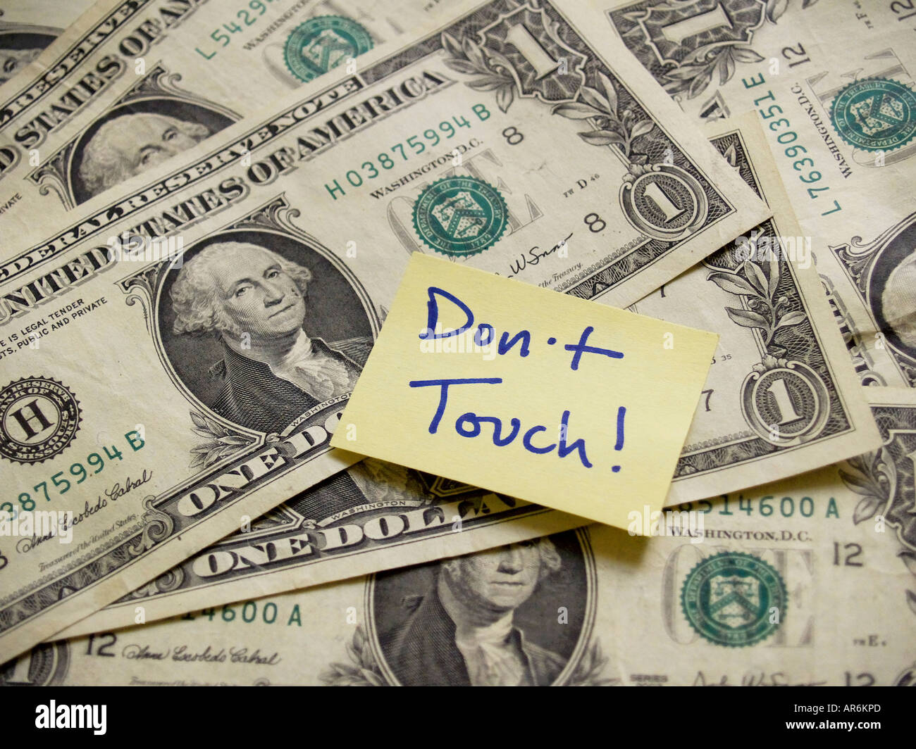 Yellow post-it sticky note containing the words DON'T TOUCH stuck on a background of dollar bills. Stock Photo