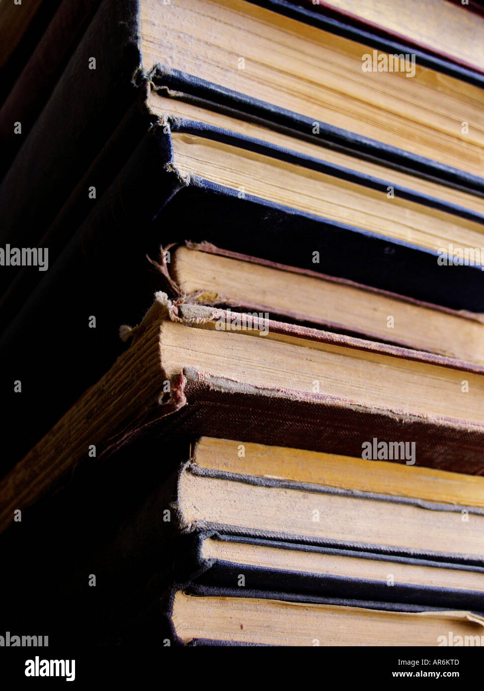 A stack of very old dusty yellowing books with decaying covers in extremely strong light and shadow. Stock Photo