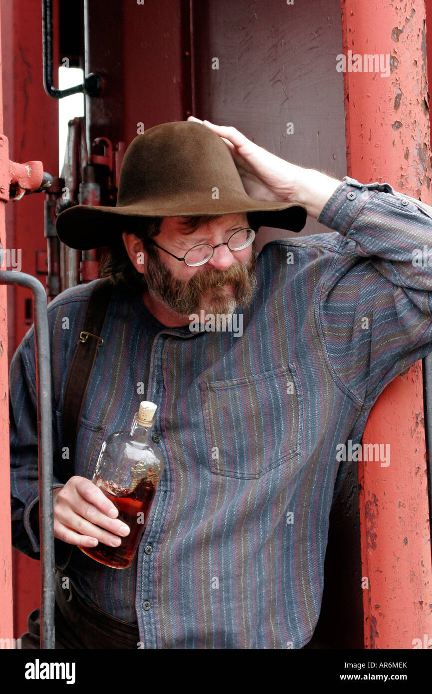 A drunk with a bottle of alcohol riding the rails of a steam train in Laona Wisconsin during a western reenactment Stock Photo