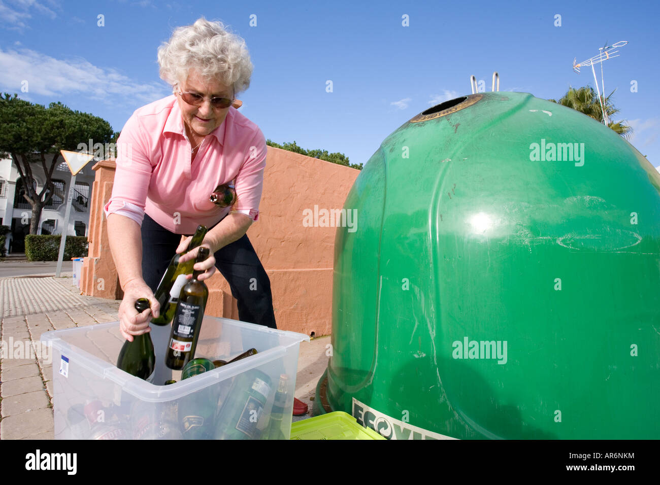 Senior woman putting empty glass bottles in to recycle bin Stock Photo