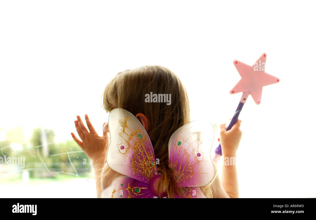 4 year old female child dressed as fairy with wand, looking out window Stock Photo
