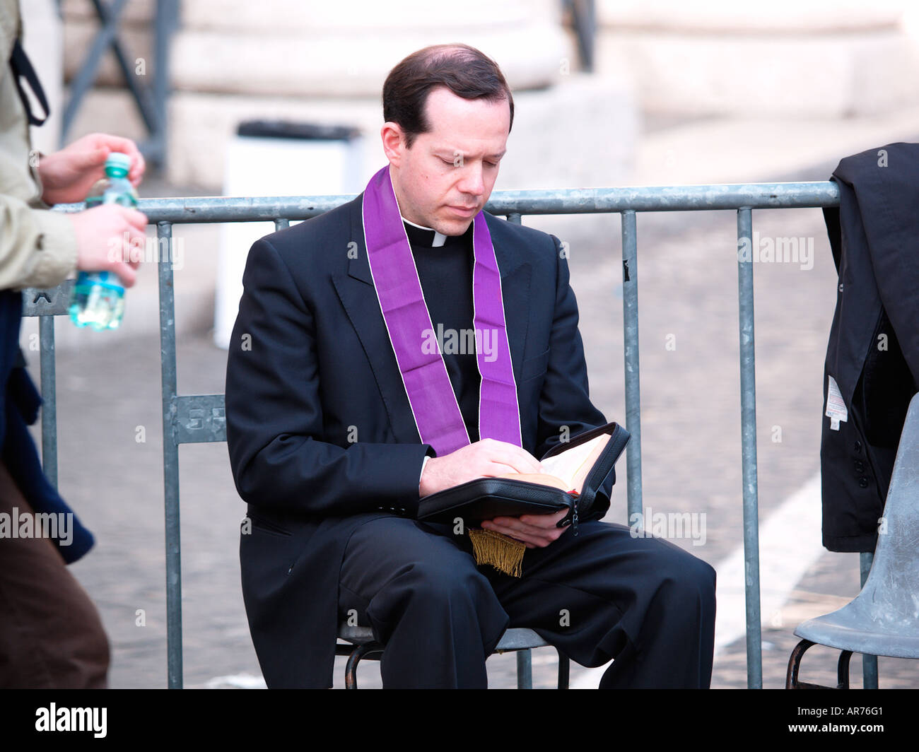 Catholic priest sat on chair in street reading bible Stock Photo Alamy