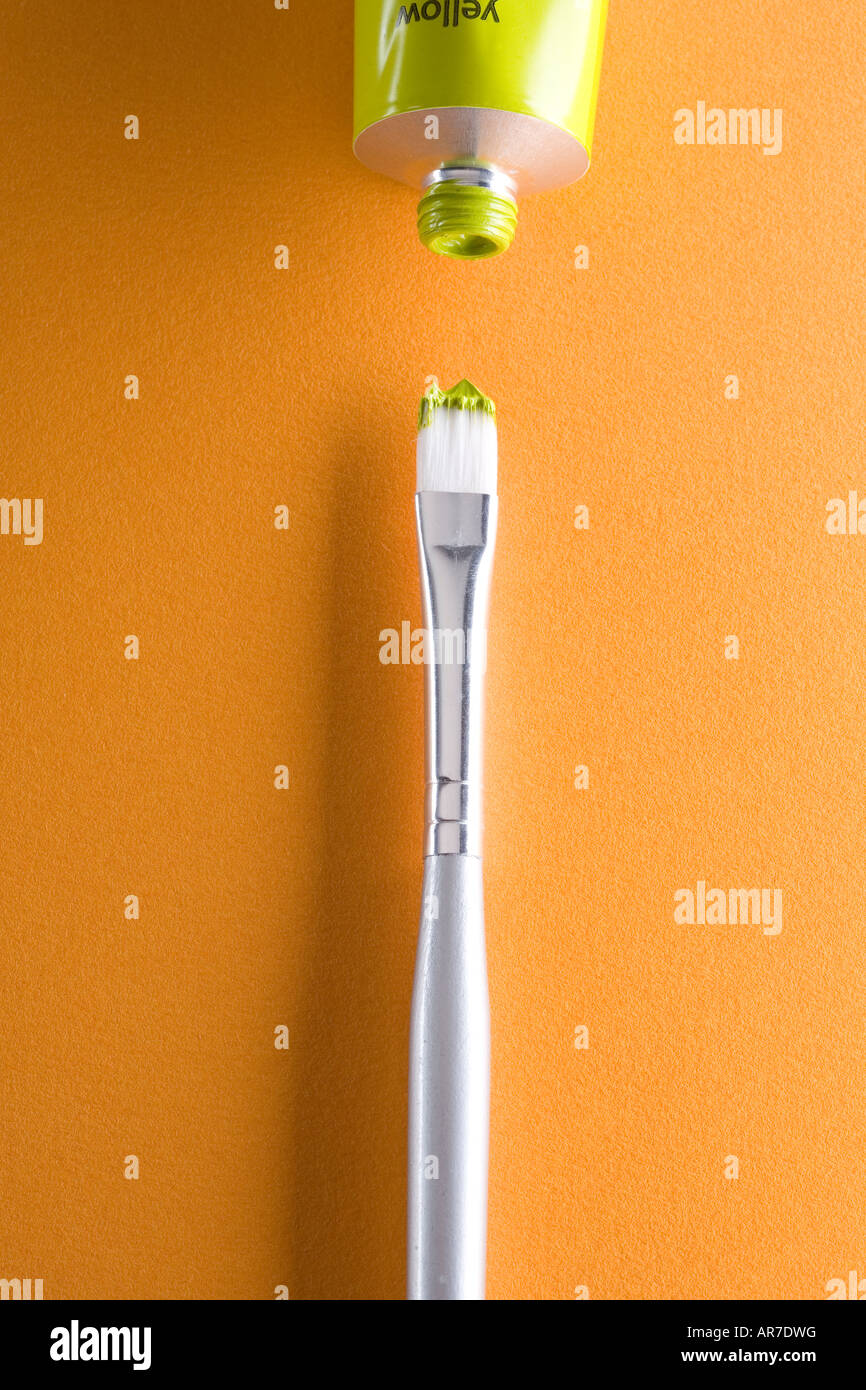Silver paint brush with dab of yellow green paint next to open tube of