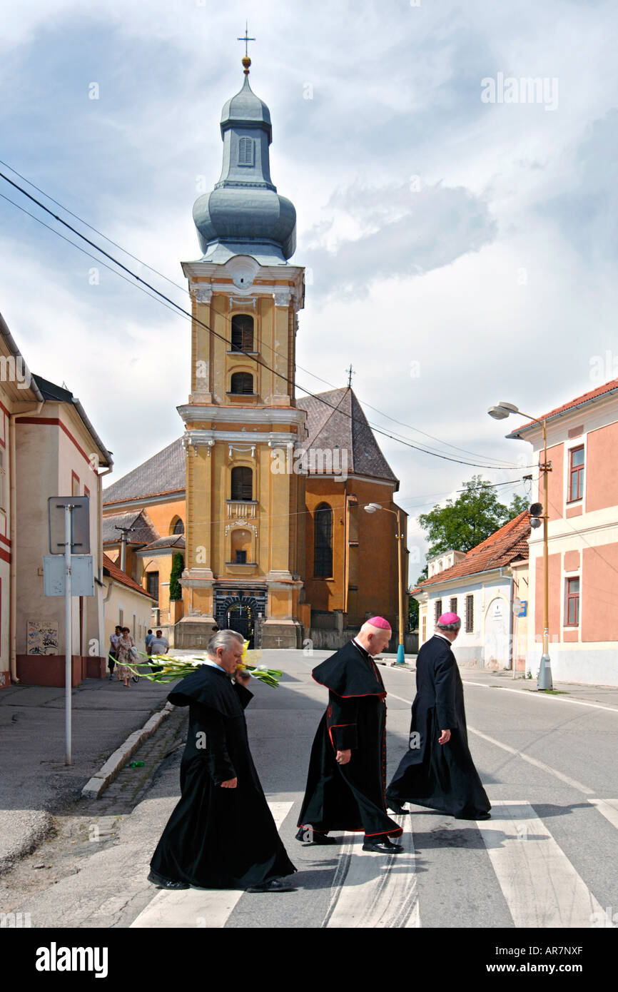 Three men of the cloth walking past a church in Roznava in eastern Slovakia. Stock Photo