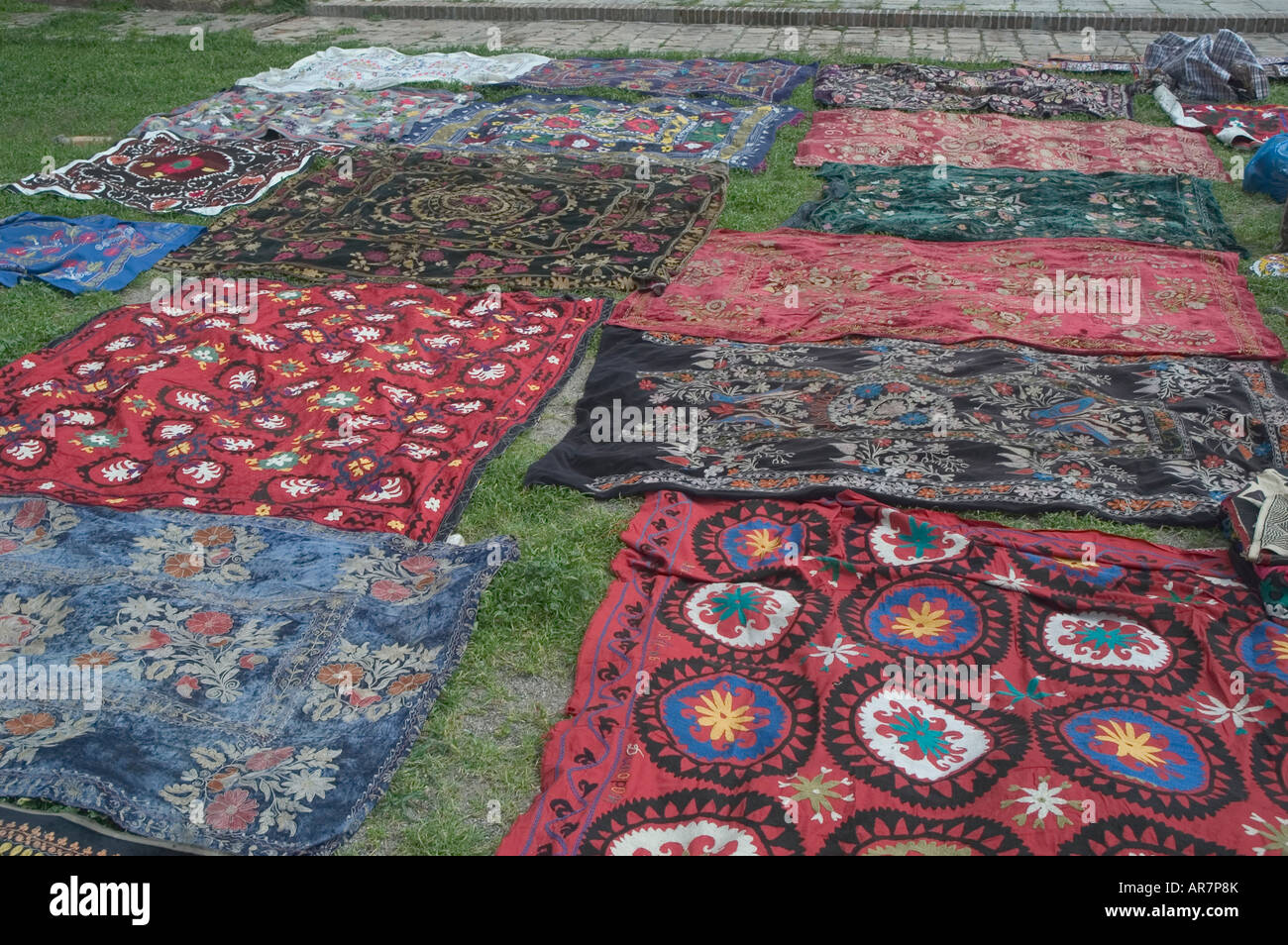 A collection of hand embroidered Suzani Textiles spread out on the ground for sale Shakhrisabz (Shakrisabs) – Uzbekistan Stock Photo