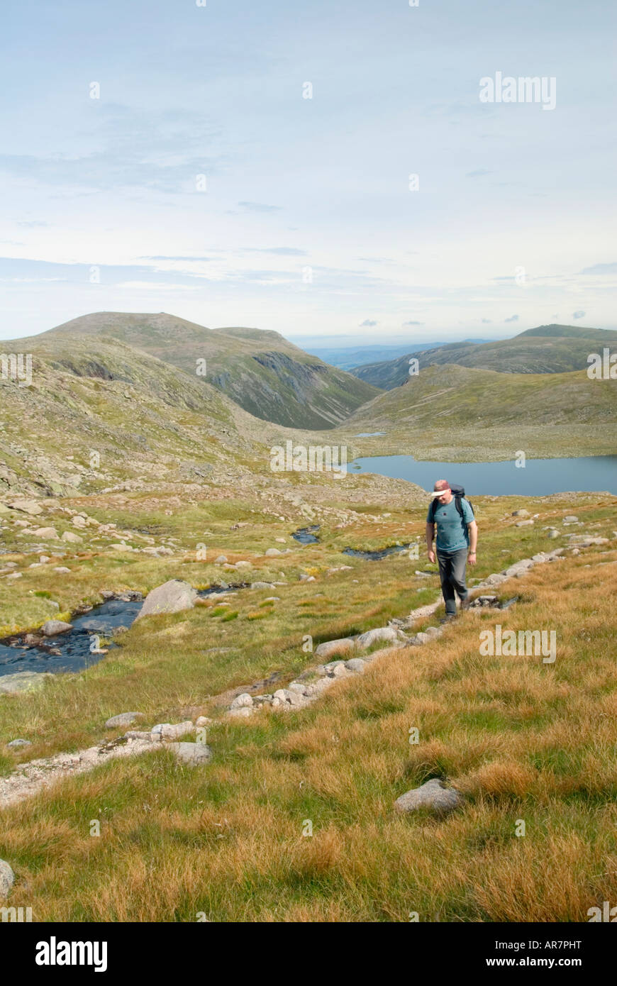 A walker makes his way to the summit of Ben Macdui, with Loch Etchechan in the background, in the Cairngorms National Park. Stock Photo