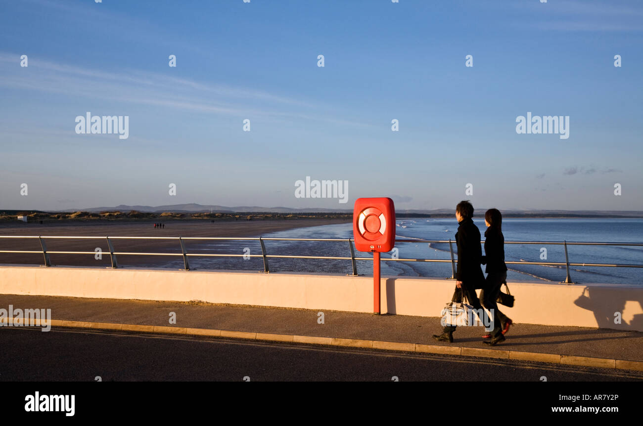 Two young people strolling along the promenade at St Andrews on a sunny evening Stock Photo