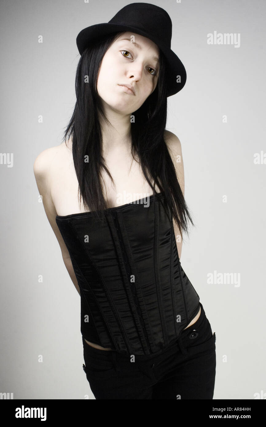 Portrait of a young brunette woman, with her arms behind her back, in a corset and a hat. Stock Photo