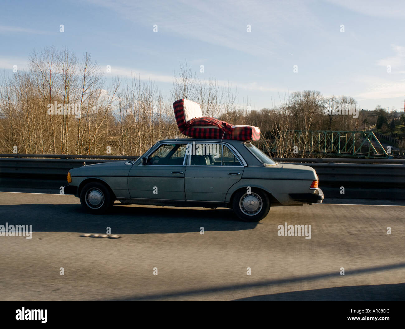 Car with a mattress on the roof driving on a freeway in