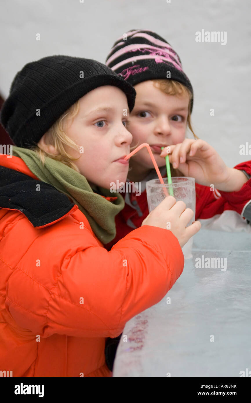 Young children in winter clothes drinking through straws from a glass made of ice in an ice bar in Norway Stock Photo