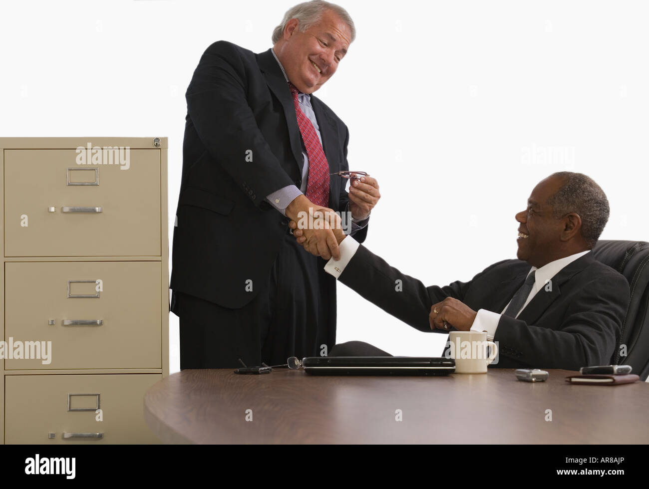 Two businessmen shaking hands and smiling in an office Stock Photo - Alamy