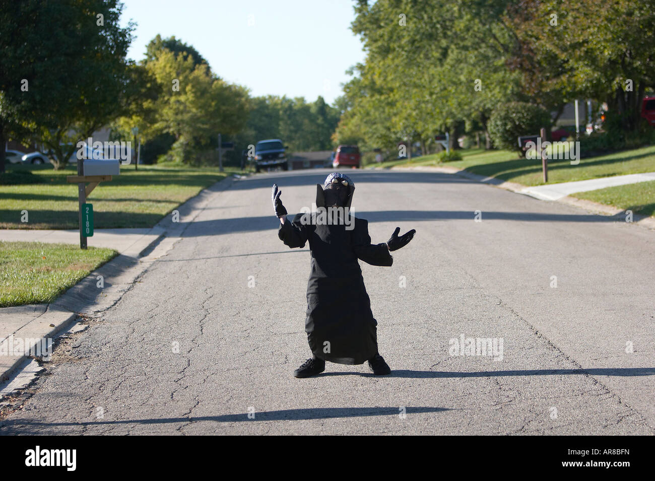 A boy in an alien costume standing in the middle of a suburban street