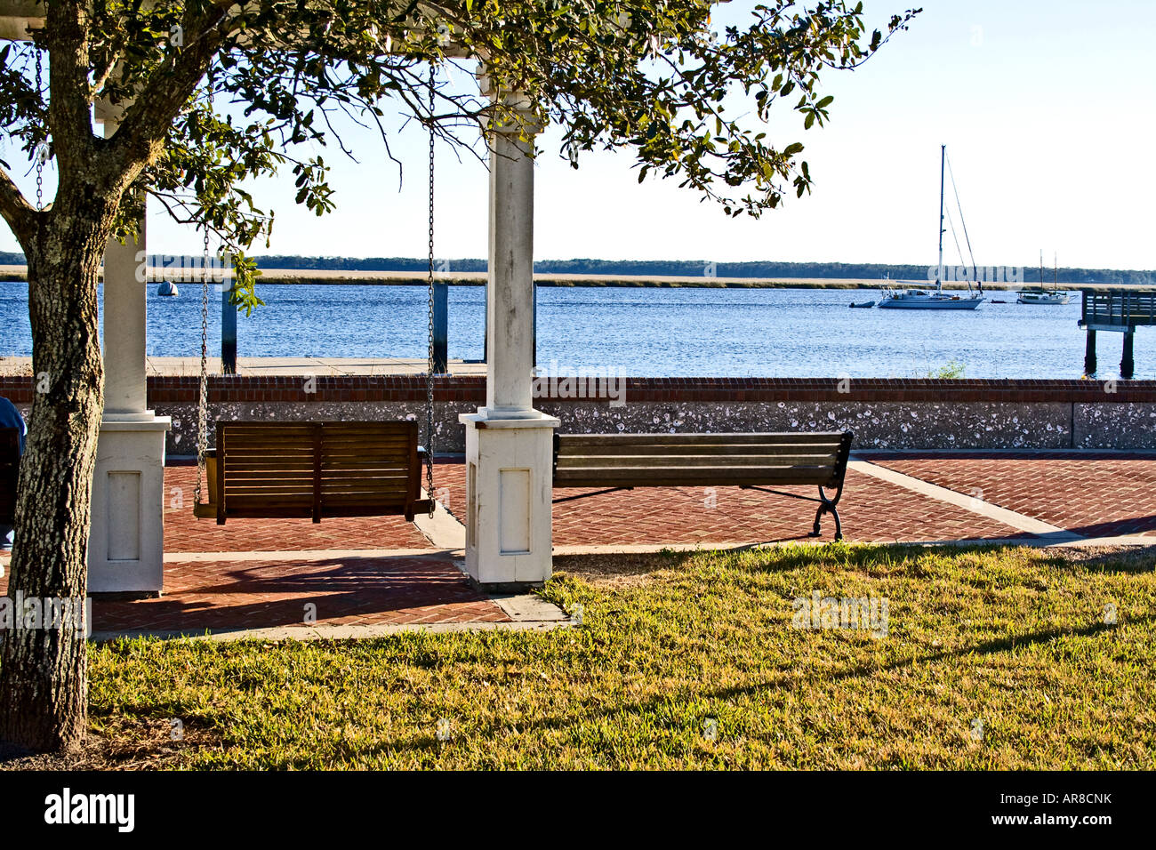 Swing an a bench overlooking a harbour with a sailboat on a calm day. Stock Photo
