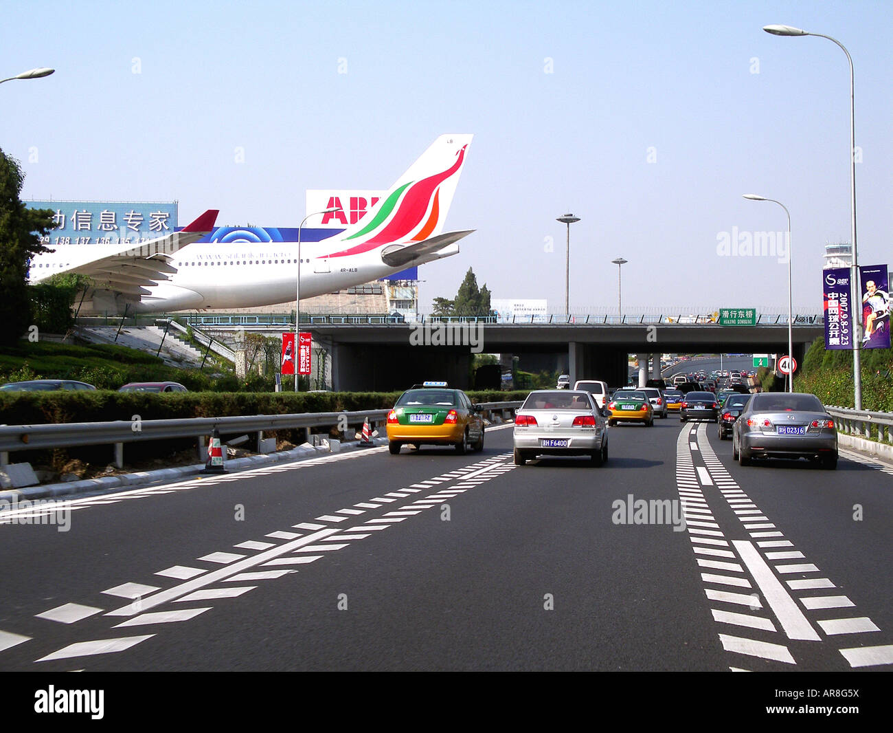 Beijing airport highway traffic, with plane crossing over-bridge. Stock Photo