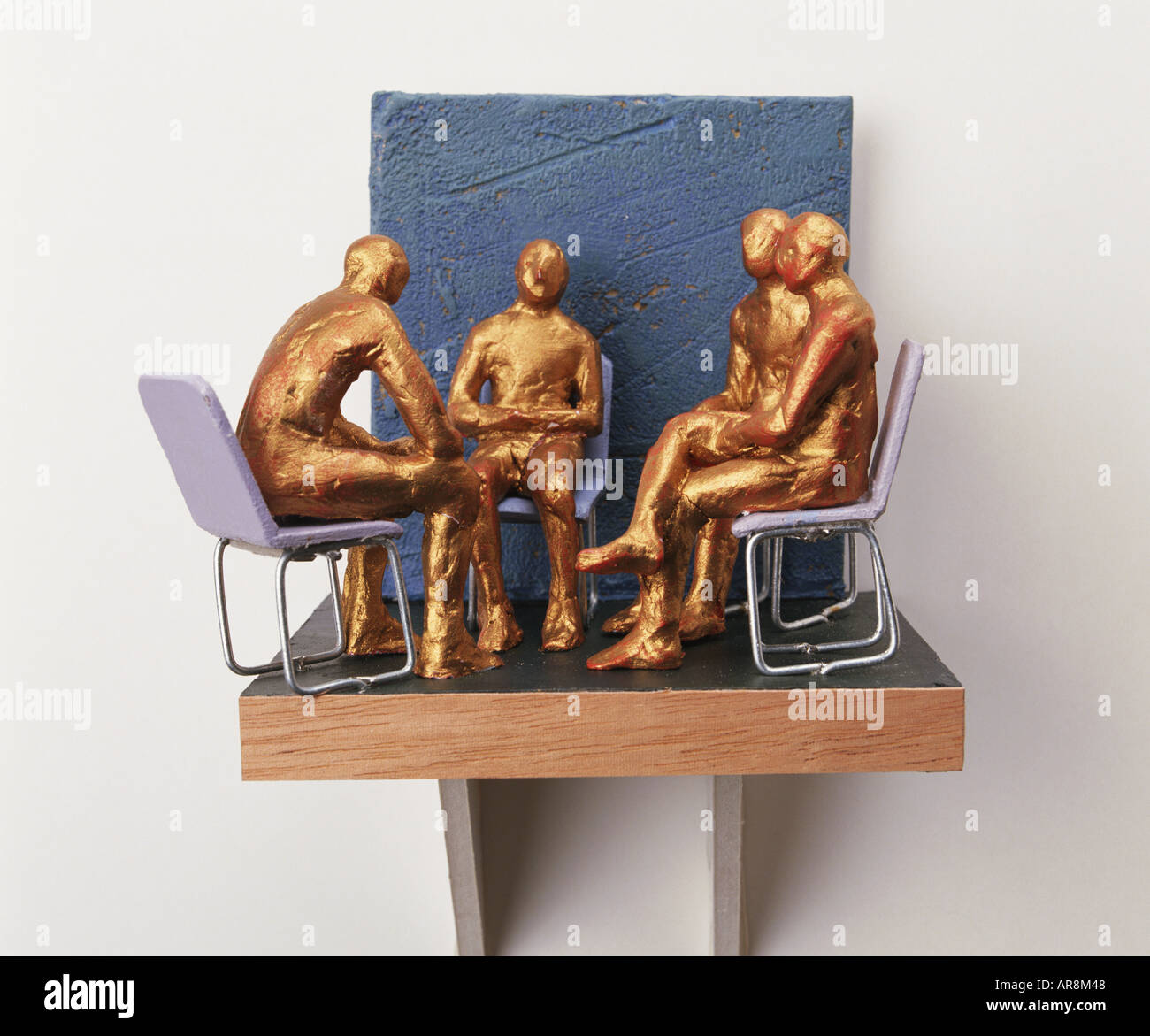 Four golden figurines sitting on chairs in a circle hires stock