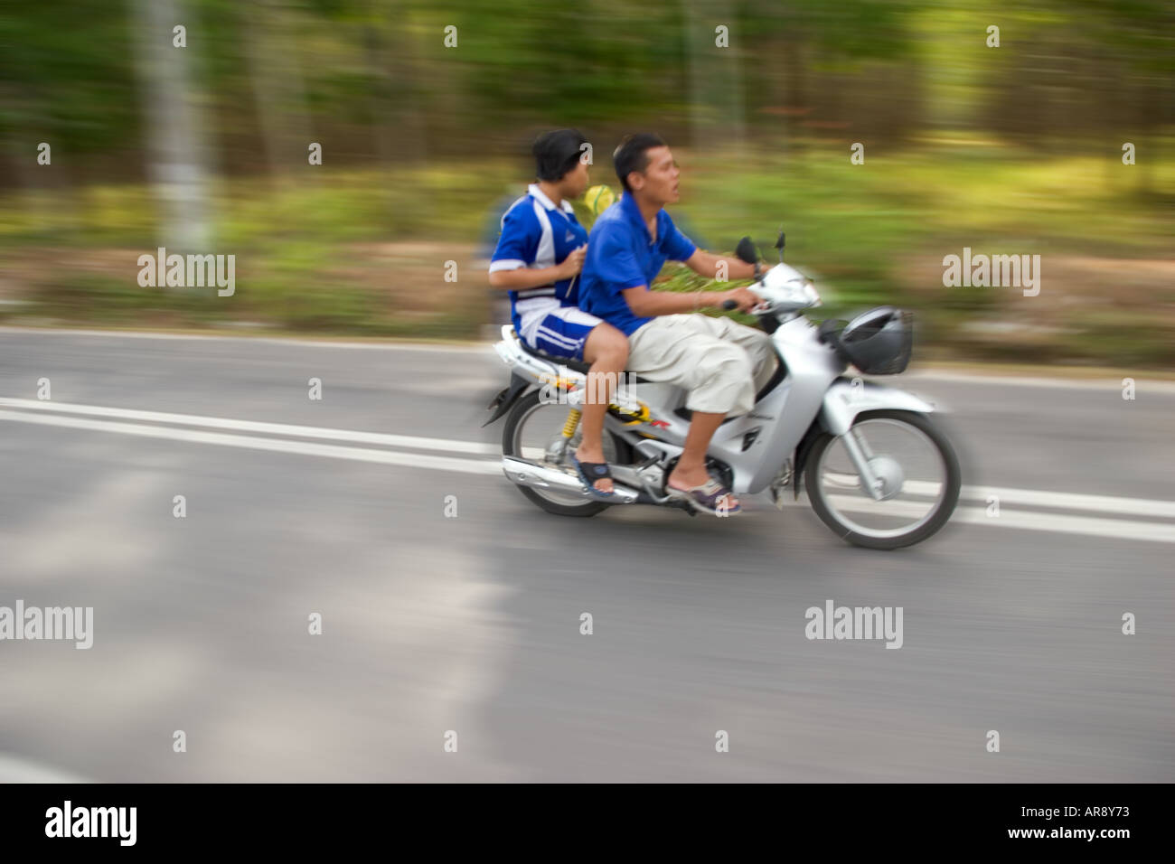 Male and female riding on a moped scooter fast along a plantation road on phuket Island, Thailand, Asia Stock Photo