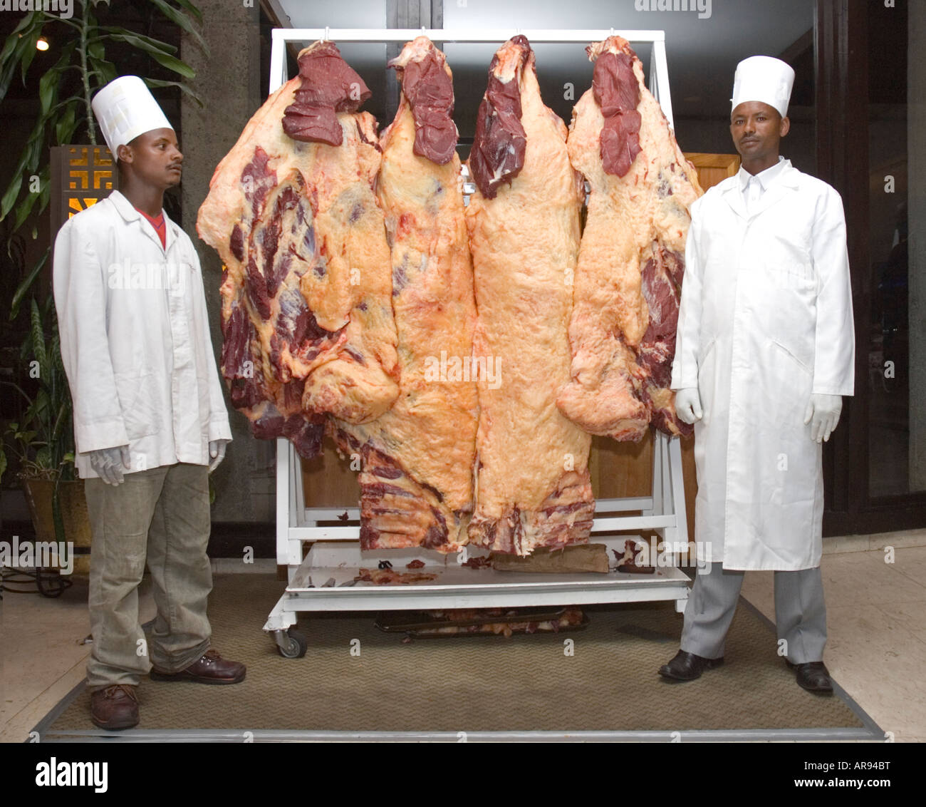 Ethiopian chefs at a wedding reception in Addis Abeba, Ethiopia with sides of raw beef hanging on a rack Stock Photo