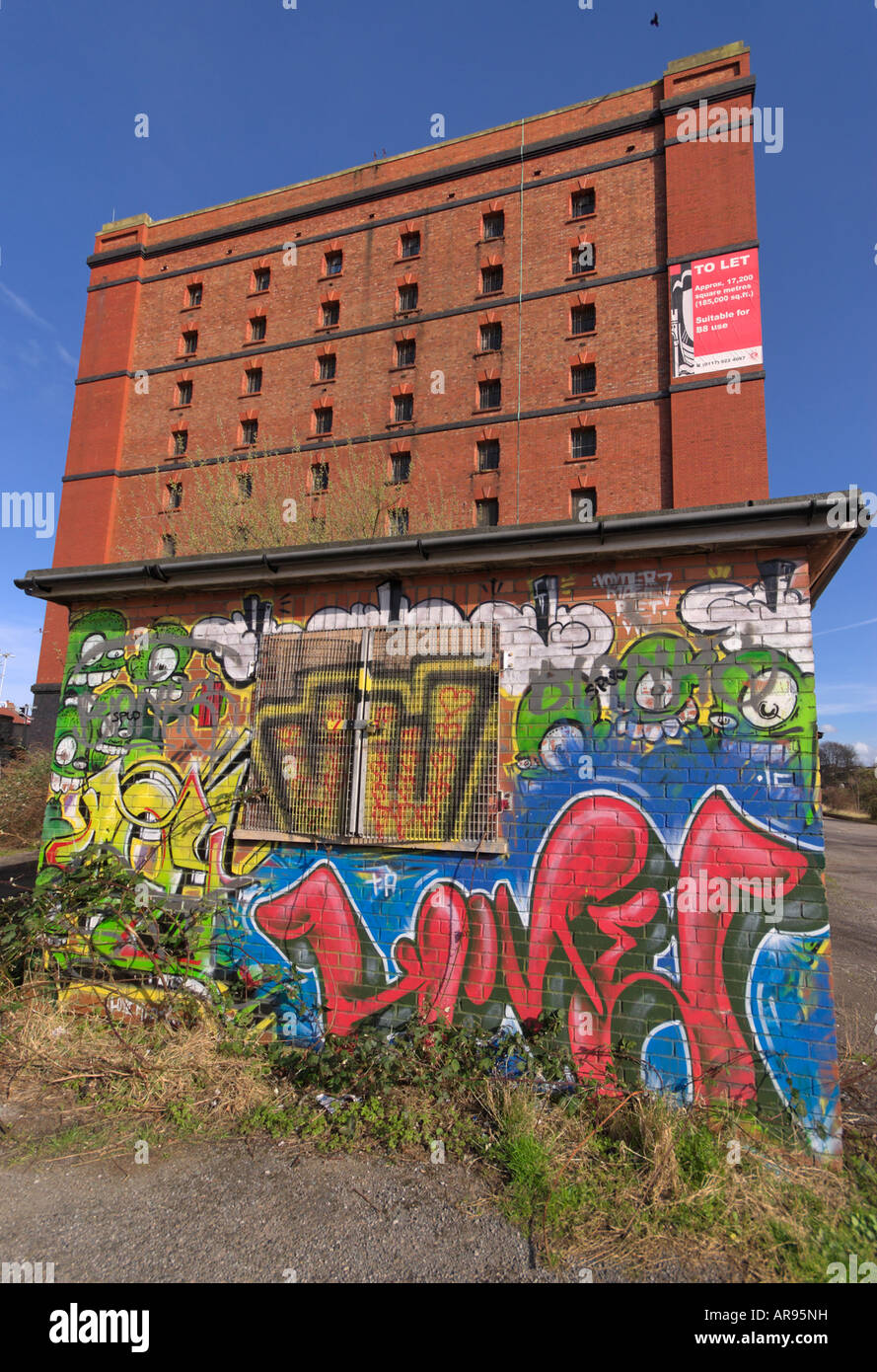 Graffiti covering the wall of a small brick built hut, with a large storage warehouse behind it in Bristol, UK Stock Photo