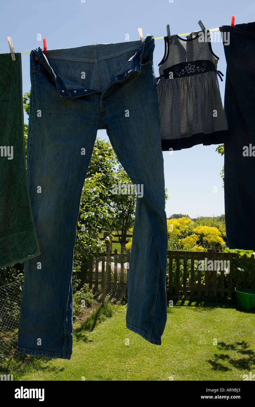 Image of a pair of large jeans hanging on a washing line next to a small babies dress Stock Photo