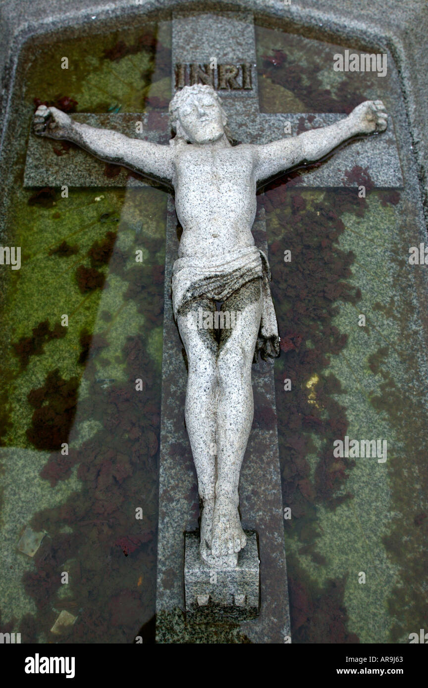 granite statue of christ crucifixtion half submerged in dirty water jesus Stock Photo