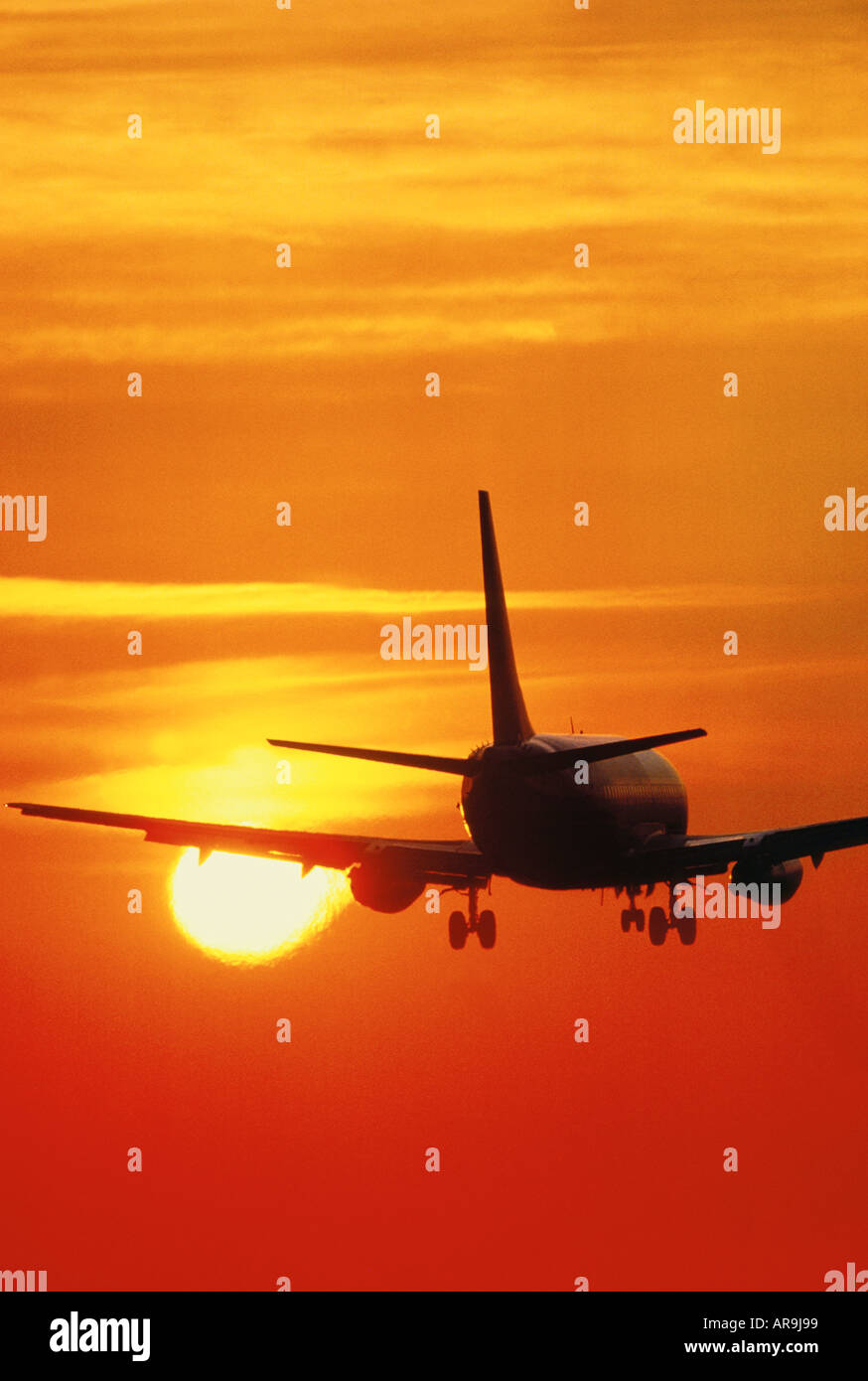 Boeing 737 in the air flying into an golden orange sky at sunset sunrise dusk silhouette Stock Photo
