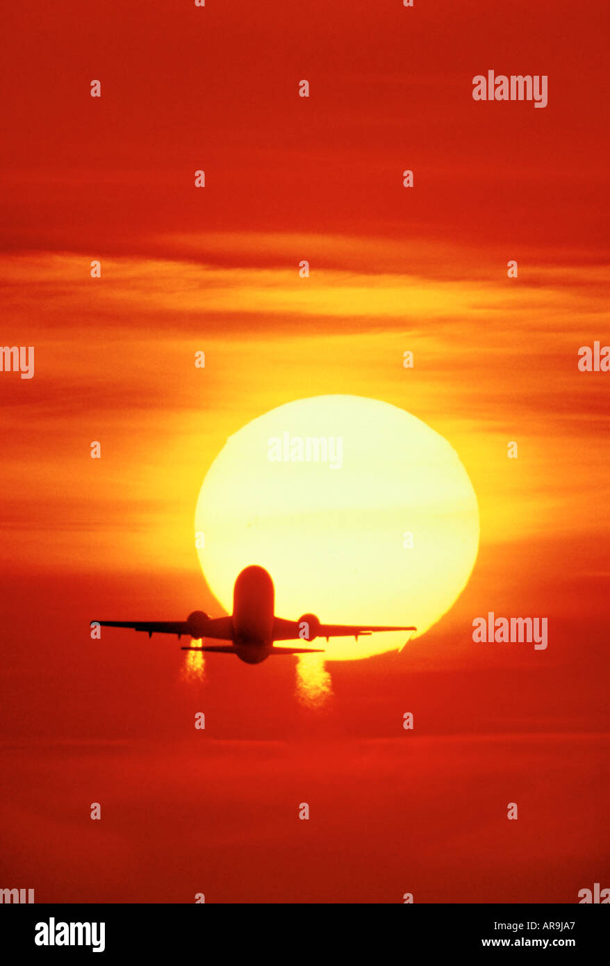 Boeing 737 in the air flying into an golden orange sky at sunset sunrise dusk showing jet thrust exhaust pollution silhouette Stock Photo