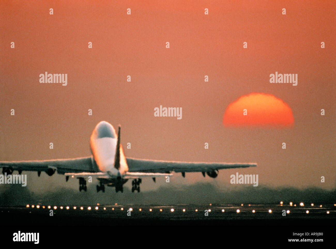 Boeing 747 jumbo jet in the air just above the runway lights flying heading into an golden orange sky at sunset sunrise dusk sho Stock Photo