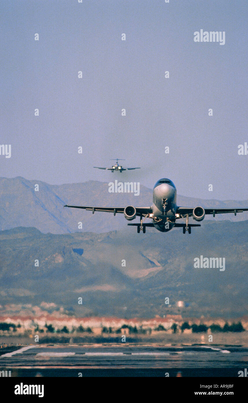 airport congestion busy traffic jet airliners landing and taking off just airborne above runway head on view with hills mountain Stock Photo